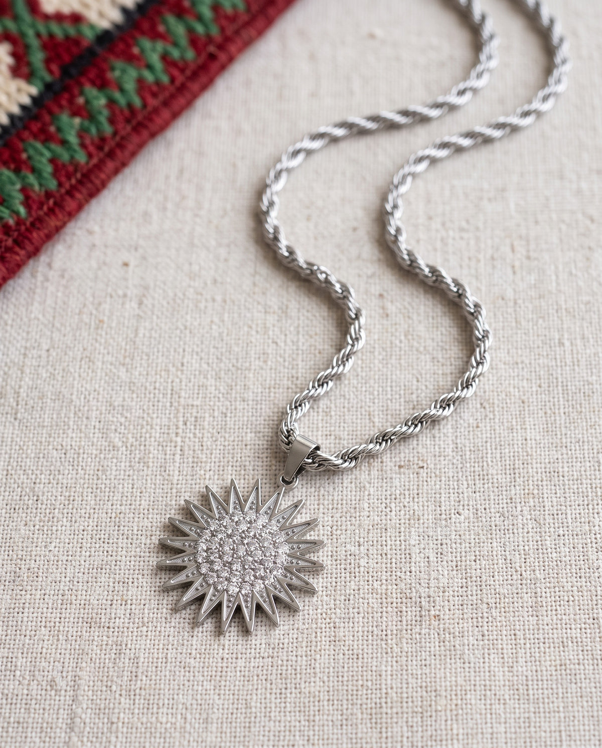 Collier Kurdistan Guerrier homme plaqué argent, pendentif soleil kurde à 21 rayons avec zircons clairs, chaîne corde, à plat sur lin avec tissu kurde